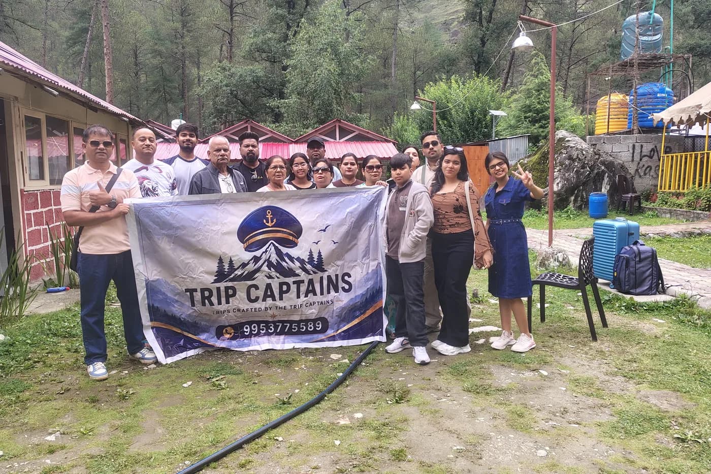 A group of about fourteen travellers outside forest cabins, holding a Trip Captains banner between them.